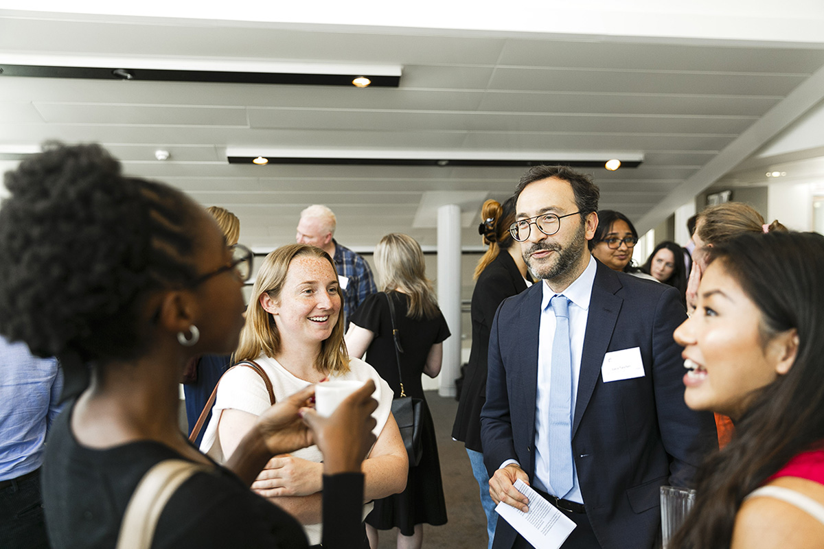 A group of four people talking at a business networking event with several people in the background