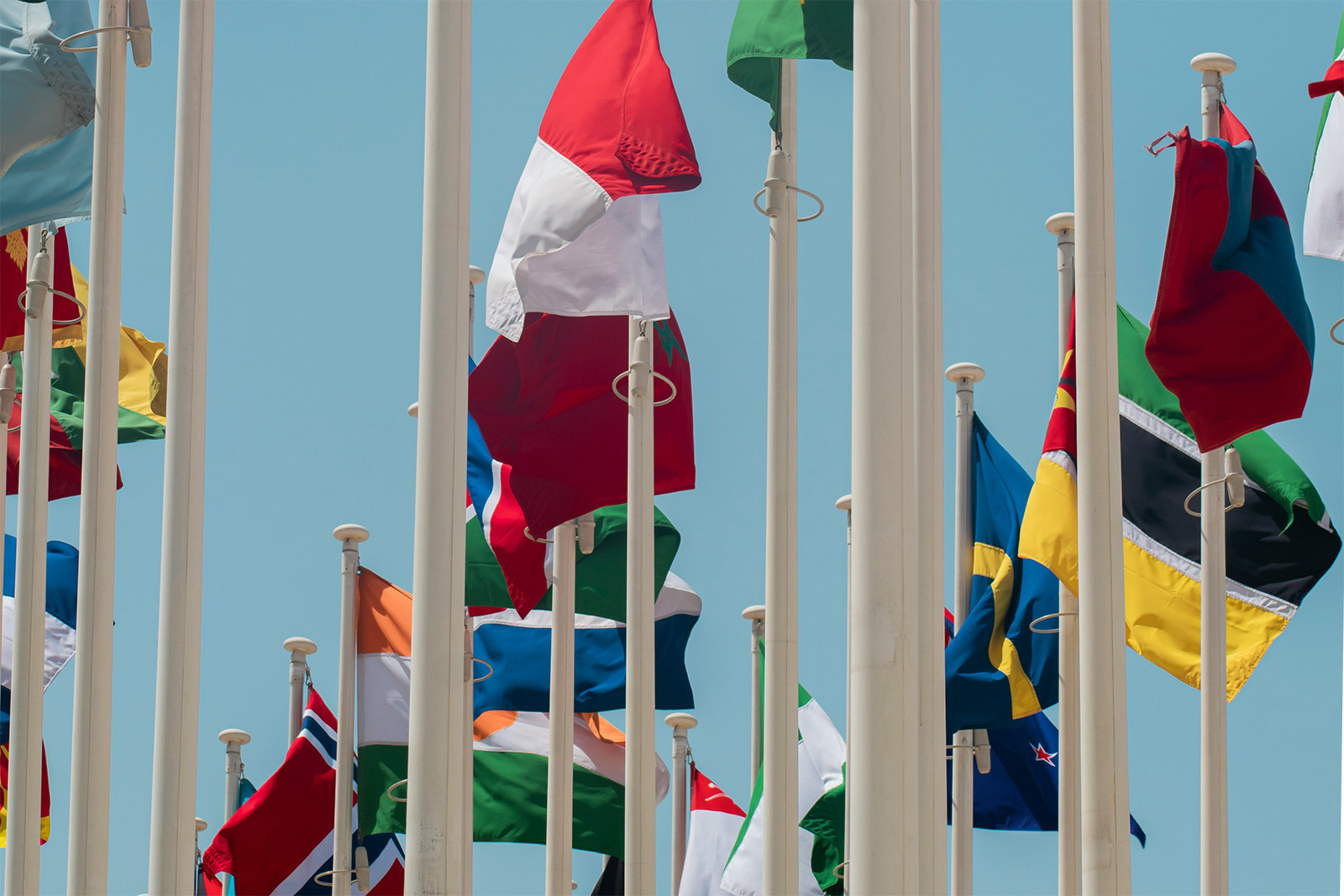 A collection of flags waving in the breeze against a clear blue sky, representing diverse nations and cultures.