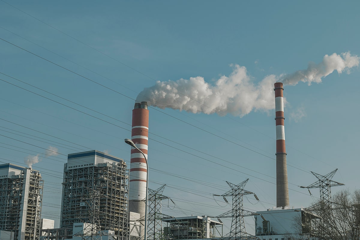 Tall chimneys emitting smoke and electricity pylons in an industrial complex.