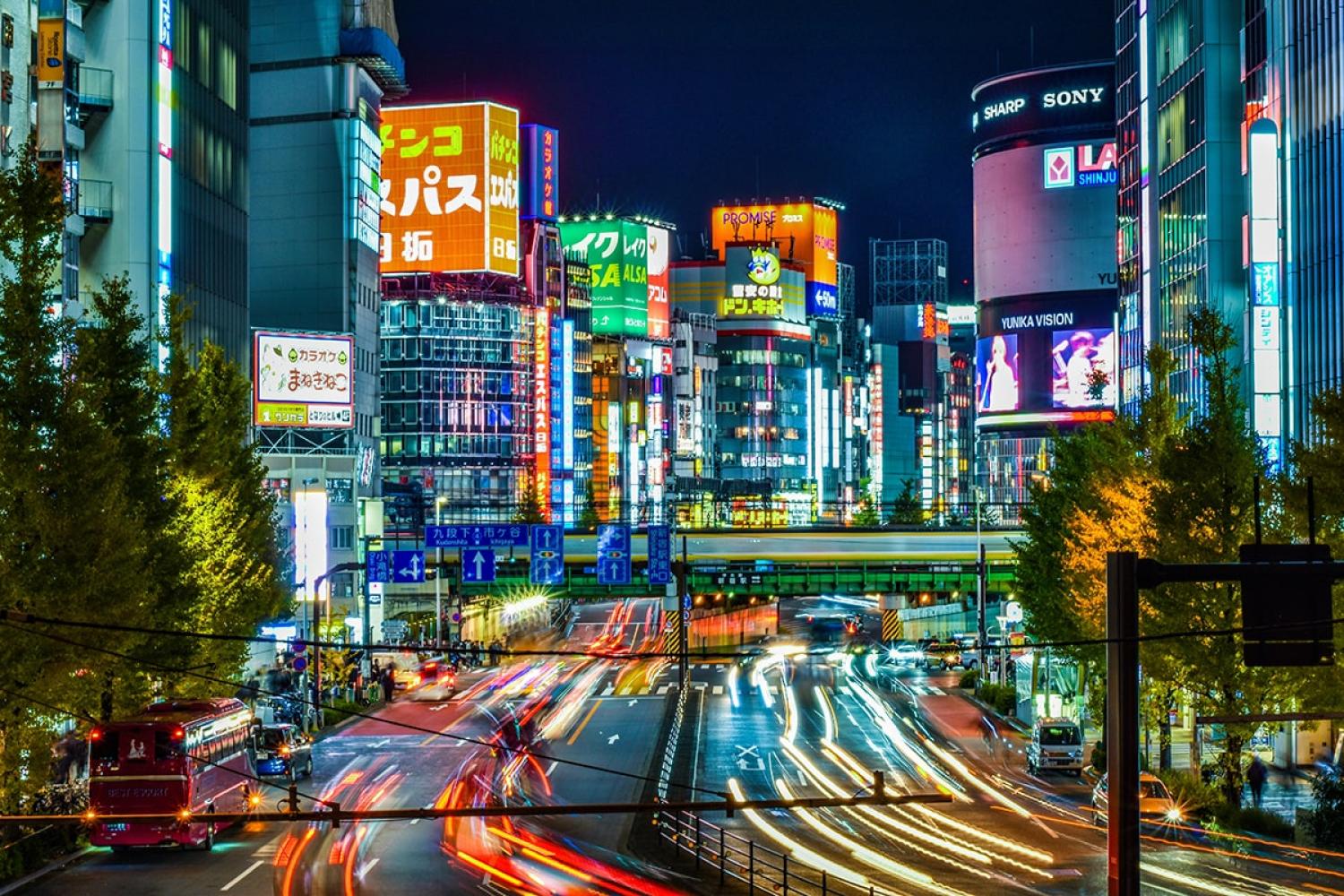 A busy street in Tokyo at night time with lots of colourful lights and advertising