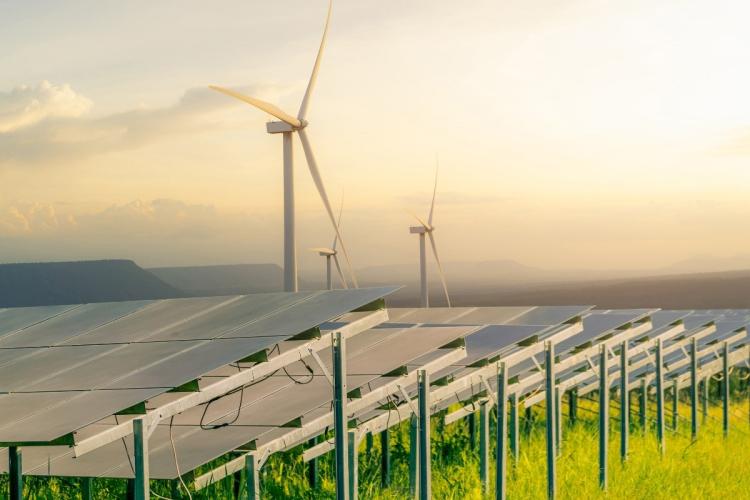A small cluster of electric wind turbines spin the background while an array of solar panels capture energy from the sun