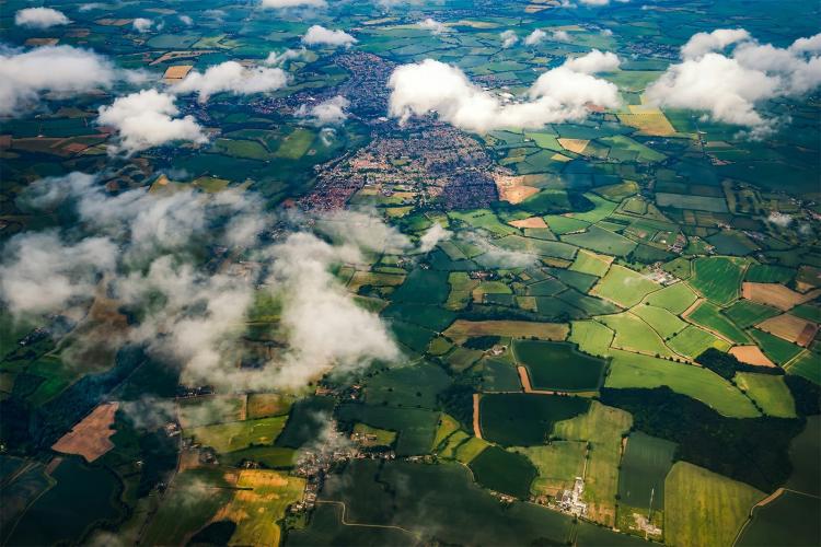 Aerial view showcasing patchwork fields beneath a sky filled with fluffy clouds.